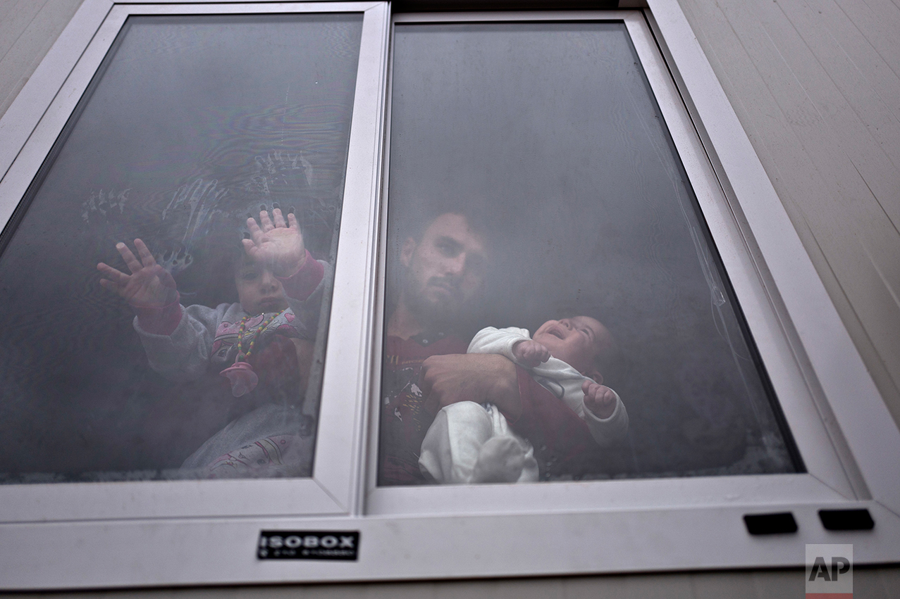  Refugee Siban Assad, 20 years old, from al-Hasaka, Syria, looks out the window of his shelter while holding his daughters, Ruba, one month, and Maldar, 1, at the refugee camp of Ritsona about 86 kilometers (53 miles) north of Athens, Wednesday, Dec.
