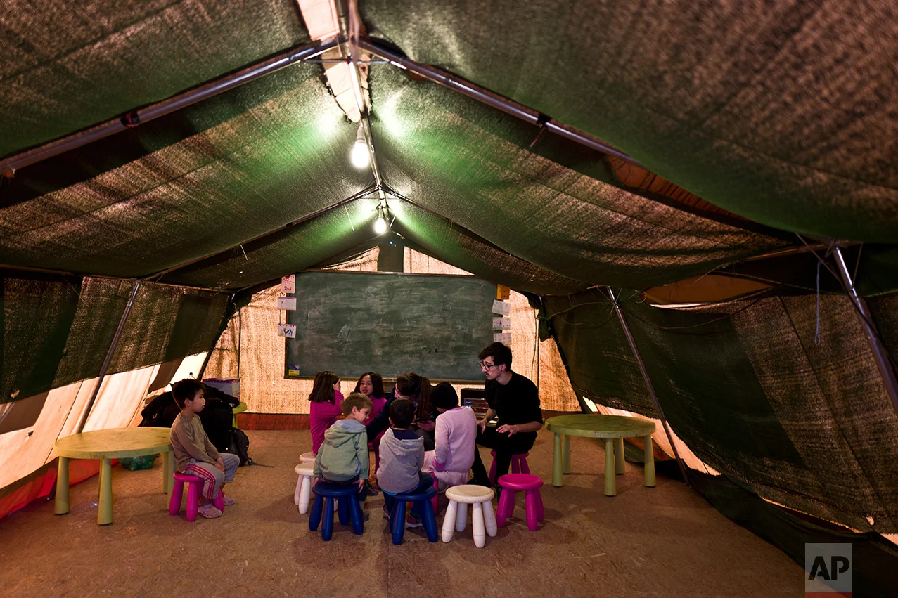 Afghan refugee children gather around two volunteering teachers during a class at a makeshift school in the refugee camp of Oinofyta about 58 kilometers (36 miles) north of Athens, Tuesday, Dec. 27, 2016. (AP Photo/Muhammed Muheisen)