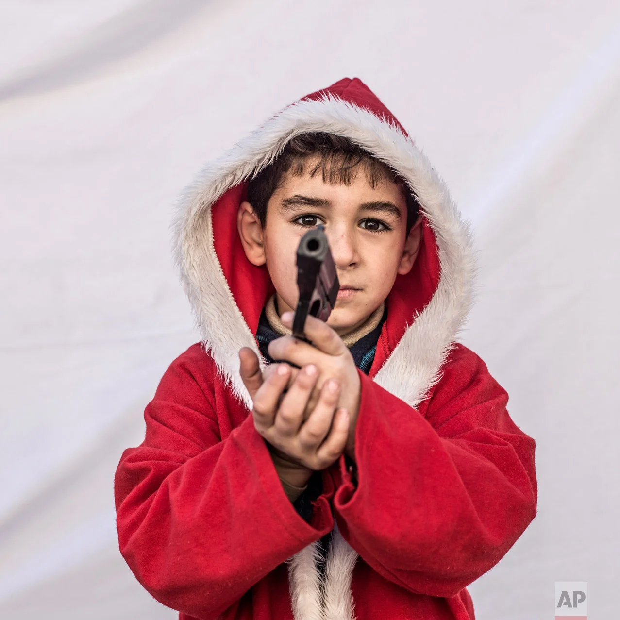 Kayaks, 7, poses for a picture holding a toy gun in a camp where Christians displaced by Islamic State militants are living, in Irbil, Iraq, Friday, Dec. 23, 2016. Iraq's Christians are marking the holiday in this camp for displaced people with a sense of worry and despair, unable to return to their towns they were forced to flee two years ago by the Islamic State group's onslaught. (AP Photo/Manu Brabo)