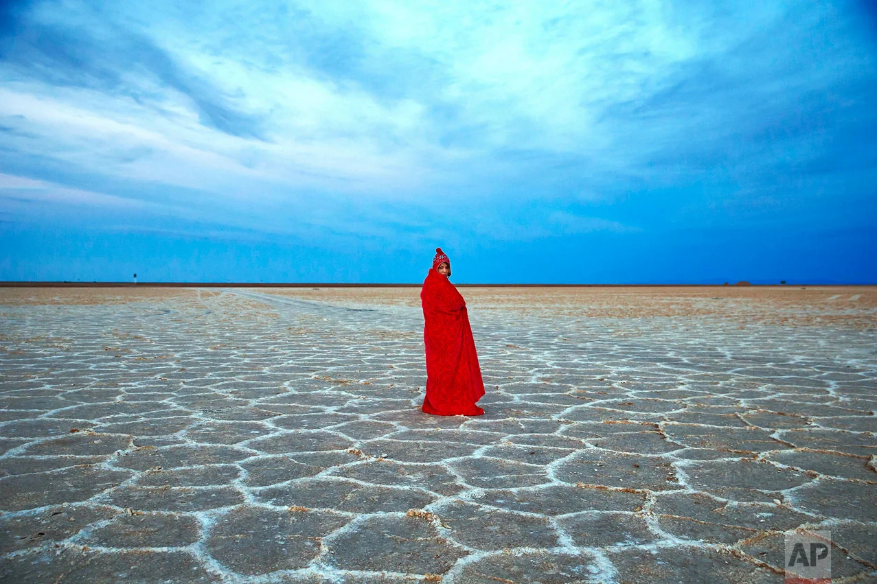 In this picture taken on Thursday, Dec. 1, 2016, an Iranian woman covers herself with a blanket due to the cold, while visiting Khour salt lake during her tour of the Mesr desert about 305 miles (500 kilometers) southeast of the capital Tehran, Iran. Deserts make up parts of Iran which have recently become tourist destinations for young Iranians looking for a break on their weekend. The increase in tourists to the desert has stimulated economic growth in the area. (AP Photo/Ebrahim Noroozi)