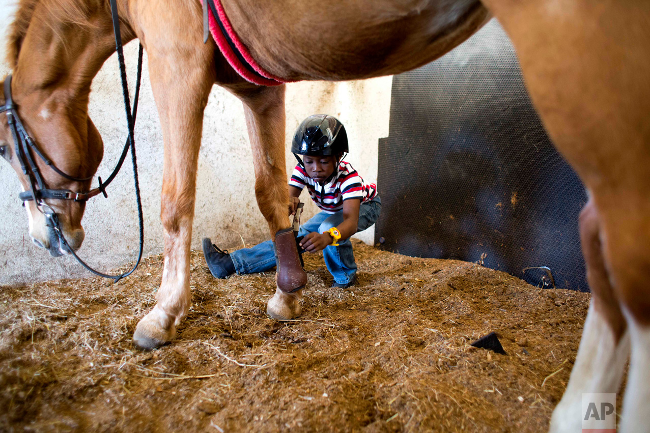 In this Jan. 7, 2017 photo, Judeley Hans Debel squats down to remove a boot from Tic Tac, holding out his prosthetic leg after his therapeutic riding lesson at the Chateaublond Equestrian Center in Petion-Ville, Haiti. Anne-Rose Schoen, who founded the equestrian center, said perhaps the most important thing about therapeutic riding is it makes youngsters happy in a country where disabled people face enormous challenges. (AP Photo/Dieu Nalio Chery)