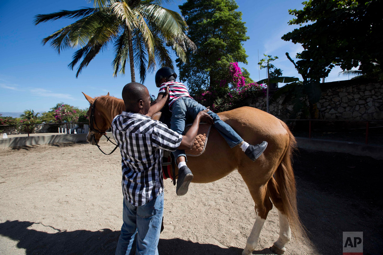 In this Jan. 7, 2017 photo, Judeley Hans Debel dismounts Tic Tac with some help from his teacher at the Chateaublond Equestrian Center in Petion-Ville, Haiti. Advocates of therapeutic riding say it improves balance, coordination and confidence with the movements of the horse mimicking pelvic motions involved in human walking. (AP Photo/Dieu Nalio Chery)