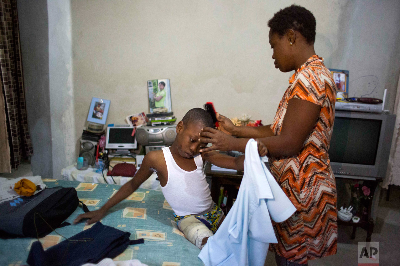 In this Jan. 10, 2017 photo, Judeley Hans Debel, who uses a prosthetic right leg, holds still as his mother Nerlande Jean Philippe readies him for school at their home in Petion-Ville, Haiti. Despite his amputated leg, Judeley enthusiastically plays soccer and other games with schoolmates and hopes to study medicine when he's older. (AP Photo/Dieu Nalio Chery)