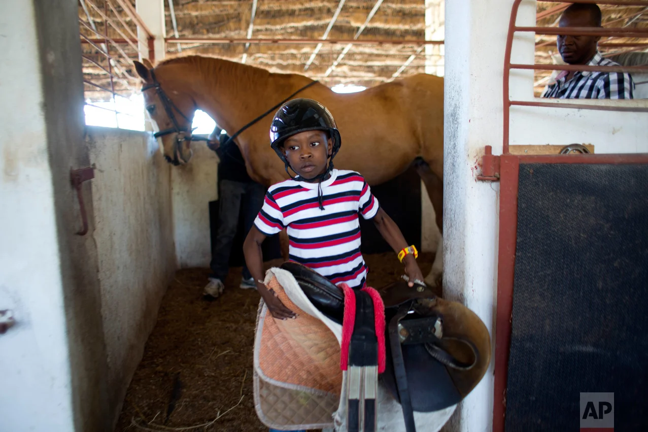 In this Jan. 7, 2017 photo, Judeley Hans Debel, who walks on a prosthetic right leg, carries his saddle away after riding Tic Tac at the Chateaublond Equestrian Center in Petion-Ville, Haiti. After riding, Judeley gives Tic Tac a bath, and is also learning how to help hoist saddles onto the animals and prepare them for rides. (AP Photo/Dieu Nalio Chery)