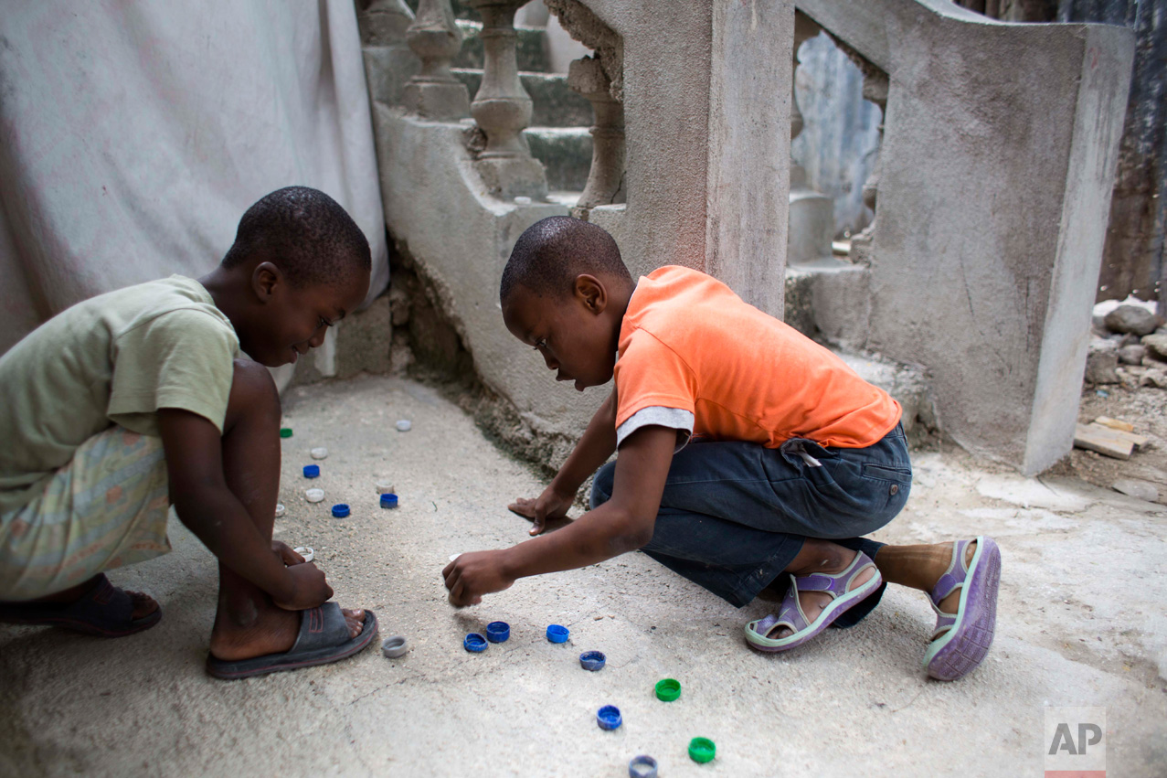 In this Jan. 8, 2017 photo, Judeley Hans Debel, right, who's right leg is a prosthesis, plays bottle cap soccer with a neighbor at his home in Petion-Ville, Haiti. Just 2 ½ years old at the time, Judeley's tiny body was pinned under earthquake rubble at his shattered concrete home in 2010. His mother dug him out and rushed him to a hospital where his leg was amputated. (AP Photo/Dieu Nalio Chery)