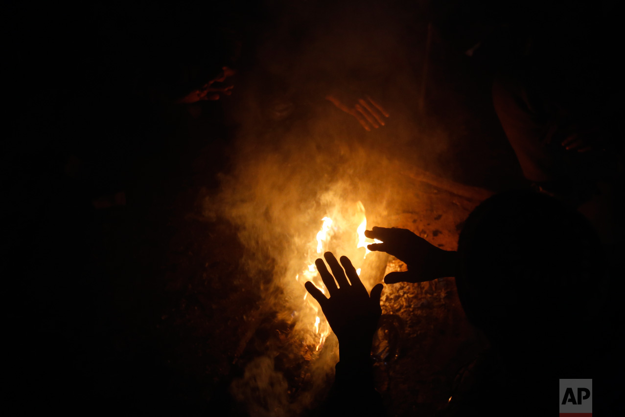 In this Thursday, Jan. 12, 2017 photo, a migrant warms up by a fire inside a crumbling warehouse that has served as a make-shift shelter for hundreds of men trying to reach Western Europe in Belgrade, Serbia. (AP Photo/Darko Vojinovic)