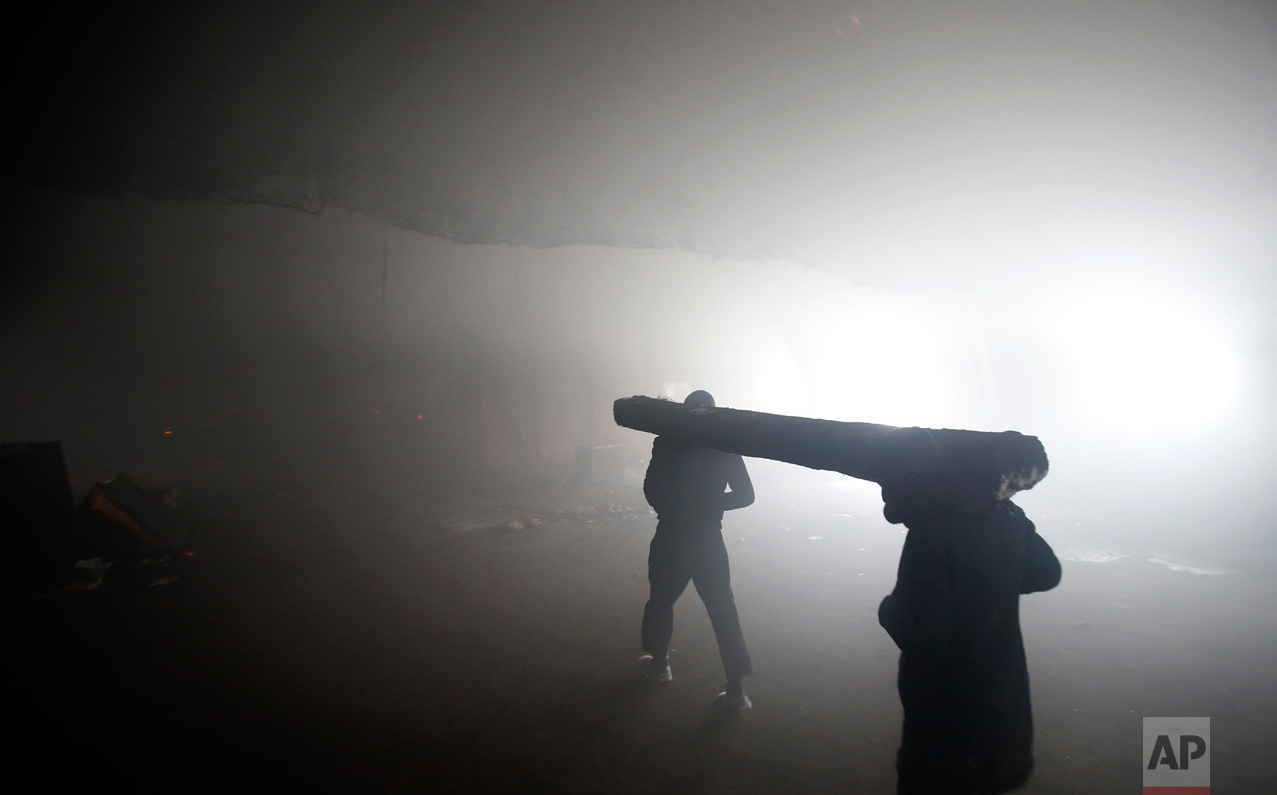 In this Thursday, Jan. 12, 2017 photo, two migrants carry a wooden railway track to use as firewood inside a crumbling warehouse that has served as a make-shift shelter for hundreds of men trying to reach Western Europe in Belgrade, Serbia. (AP Photo/Darko Vojinovic)