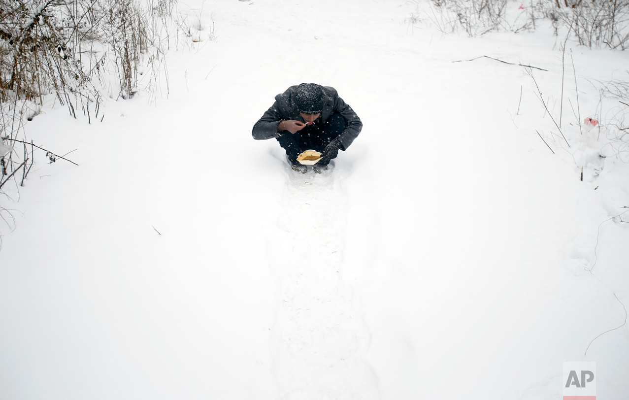 In this Wednesday, Jan. 11, 2017 photo, a migrant eats donated food in front of an abandoned warehouse in Belgrade, Serbia. (AP Photo/Darko Vojinovic)
