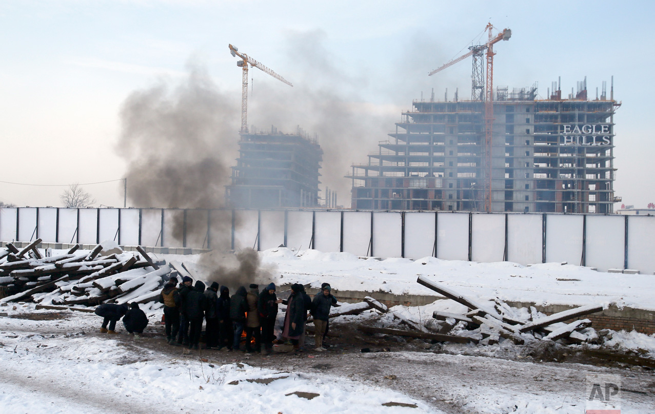 In this Tuesday, Jan. 10, 2017 photo, migrants warms themselves up by a fire next to a crumbling warehouse that has served as a make-shift shelter for hundreds of men trying to reach Western Europe in Belgrade, Serbia. Wrapped in blankets, people huddled next to each other desperately trying to keep warm by the fires they lit inside and outside the building. (AP Photo/Darko Vojinovic)
