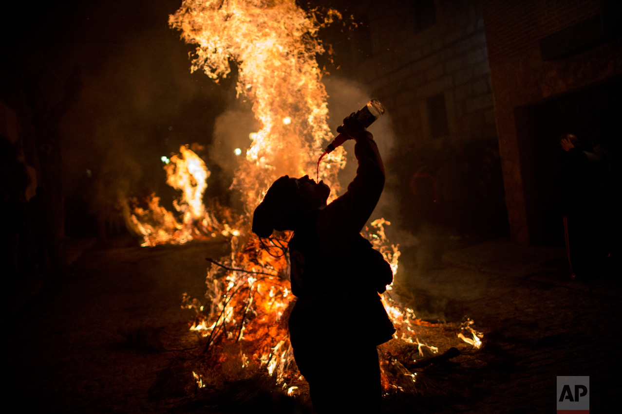 A woman drinks wine man next to a bonfire as part of a ritual in honor of Saint Anthony the Abbot, the patron saint of domestic animals, in San Bartolome de Pinares, about 100 km west of Madrid, Spain on Monday, Jan. 16, 2017. (AP Photo/Emilio Morenatti)