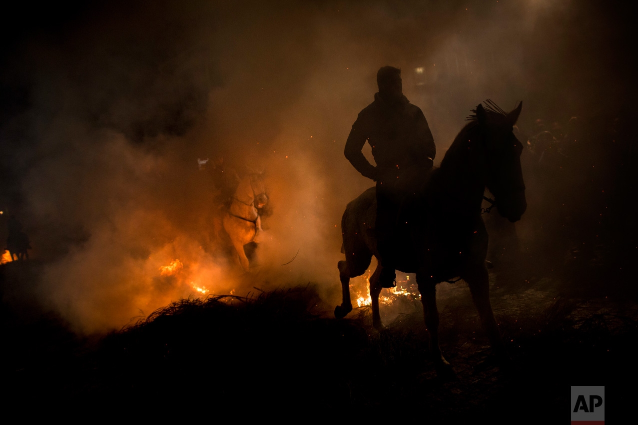 Men ride horses through a bonfire as part of a ritual in honor of Saint Anthony the Abbot, the patron saint of domestic animals, in San Bartolome de Pinares, about 100 km west of Madrid, Spain on Monday, Jan. 16, 2017. (AP Photo/Emilio Morenatti)
