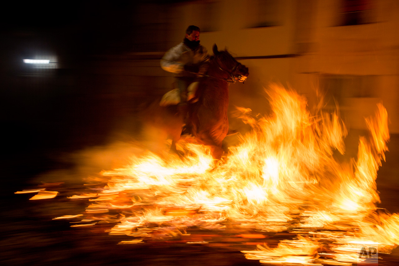A man rides a horse through a bonfire as part of a ritual in honor of Saint Anthony the Abbot, the patron saint of domestic animals, in San Bartolome de Pinares, about 100 km west of Madrid, Spain on Monday, Jan. 16, 2017. On the eve of Saint Anthony's Day, hundreds ride their horses through the narrow cobblestone streets of the small village of San Bartolome during the "Luminarias," a tradition that dates back 500 years and is meant to purify the animals with the smoke of the bonfires and protect them for the year to come. (AP Photo/Emilio Morenatti)