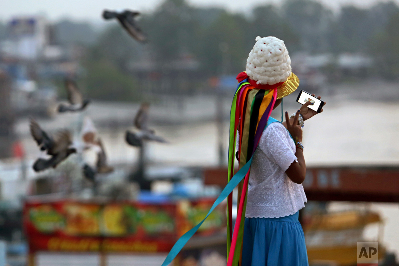 This Dec. 25, 2016 photo shows a girl in costume taking a selfie at the port in the fishing town Braganca, Para state, Brazil. This small city in northern Brazil pays tribute to St. Benedict with dance, horse competition and colorful costume. (AP Photo/Eraldo Peres)