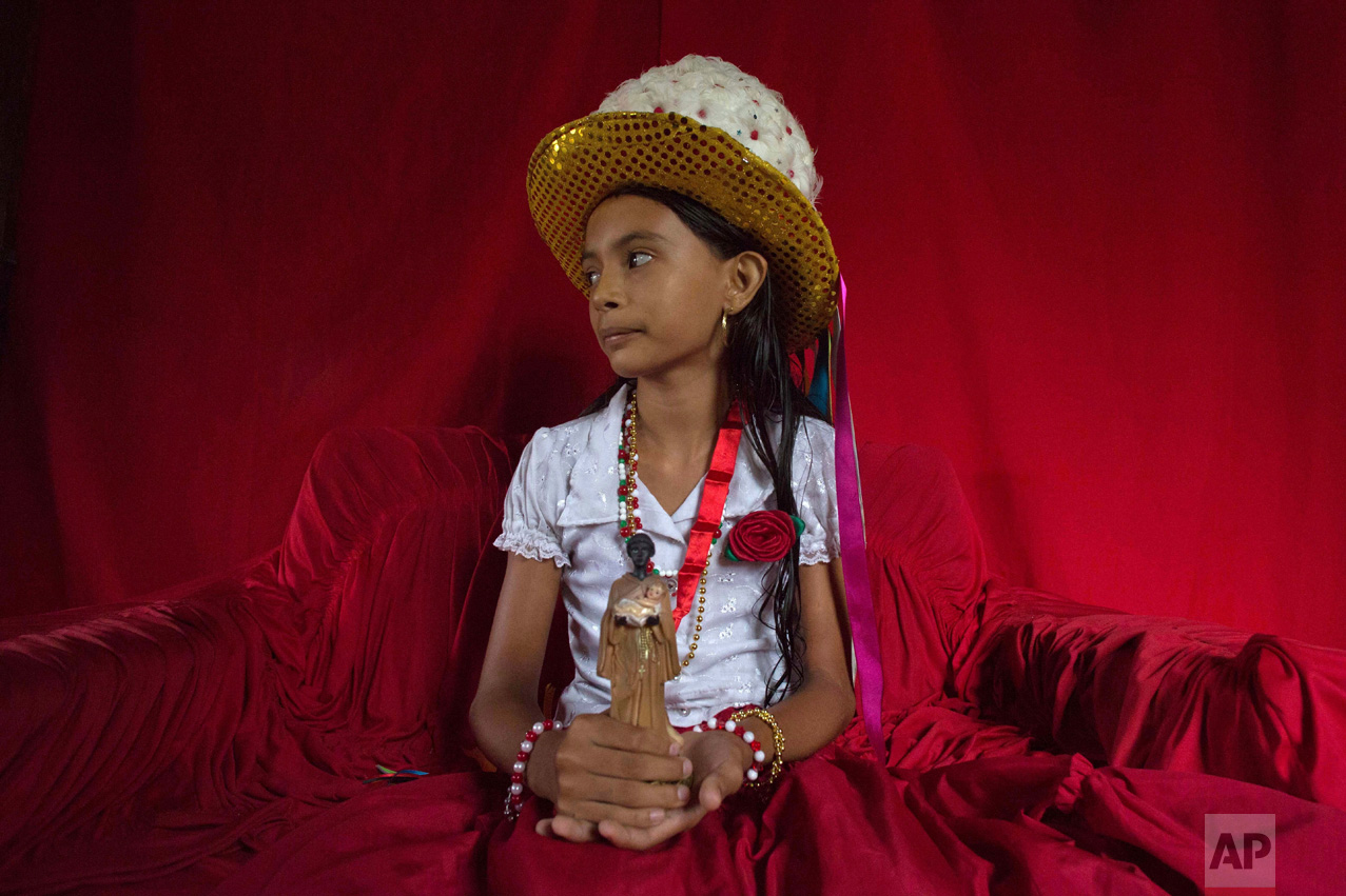 This Dec. 19, 2016 photo shows Sabrina Correia Aviz holding a statuette of St. Benedict inside her home, before the start of Marujada religious celebrations in the fishing town of Braganca, Brazil. Started in 1798, the Marujada religious celebration mixes indigenous, African and Portuguese traditions. (AP Photo/Eraldo Peres)