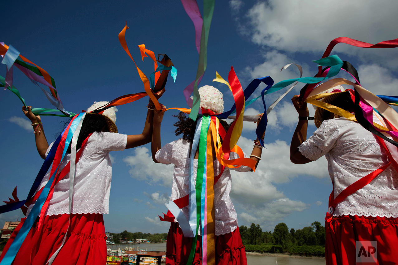 This Dec. 26, 2016 photo shows women at the port wearing feathered hats with multi-colored ribbons before the start of a procession honoring Saint Benedict during Marujada religious celebrations in the fishing town of Braganca, Brazil. Locals say the annual celebration, which started in 1798, is a way to show appreciation and make good on promises for miracles received. (AP Photo/Eraldo Peres)
