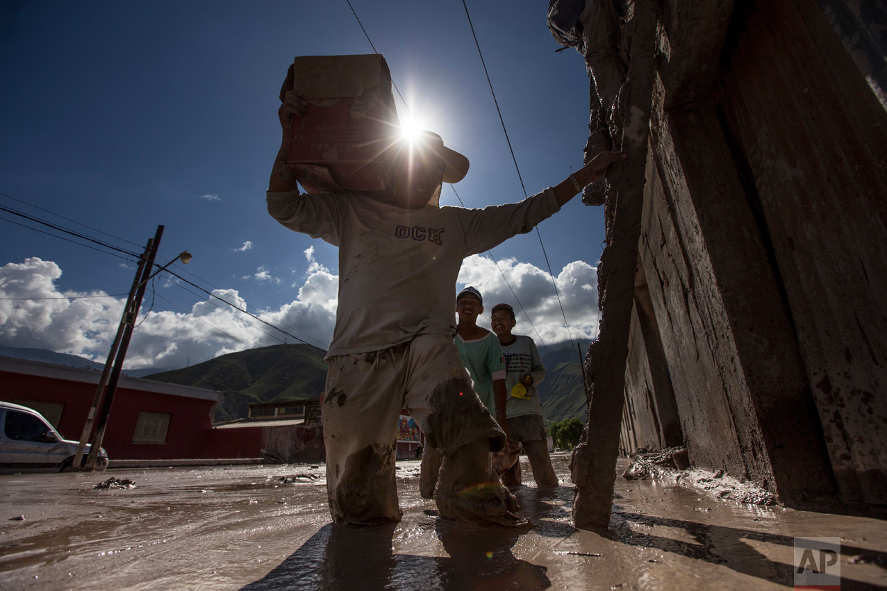 In this Jan. 13, 2017 photo, residents carry their belonging to the roofs of their mud flooded homes in the town of Volcan, Jujuy province, Argentina. Authorities declared the area a disaster zone after the town was hit by a mudslide one week ago, that covered it in a thick layer of mud. (Gianni Bulacio/Infoto via AP)