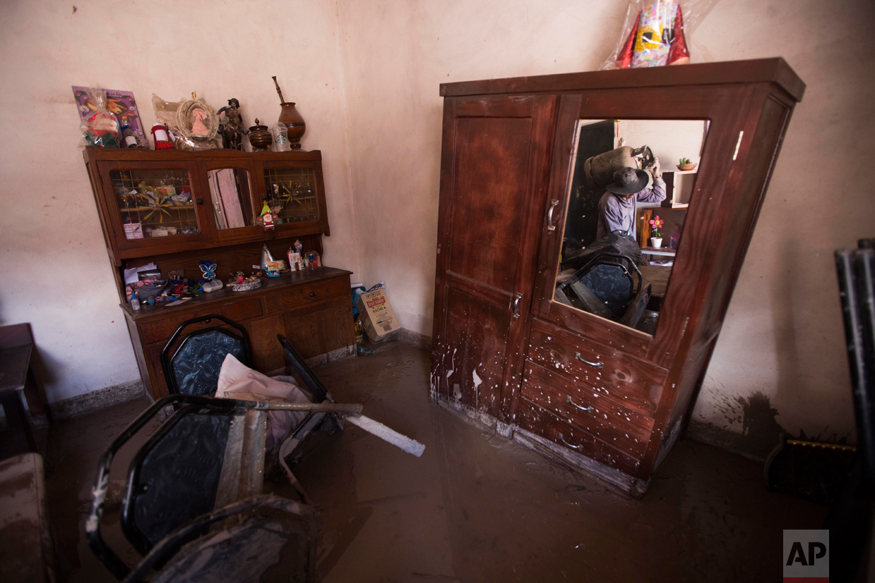 In this Jan. 13, 2017 photo, a resident carries a gas cylinder as he rescues items from his mud damaged home in the town of Volcan, Jujuy province, Argentina, Monday. The town which was hit by a mudslide one week ago, has forced the evacuation on most of its residents. Several are refusing to go, not willing to leave their belongings behind, while others help in the recovery effort. (Gianni Bulacio/Infoto via AP)