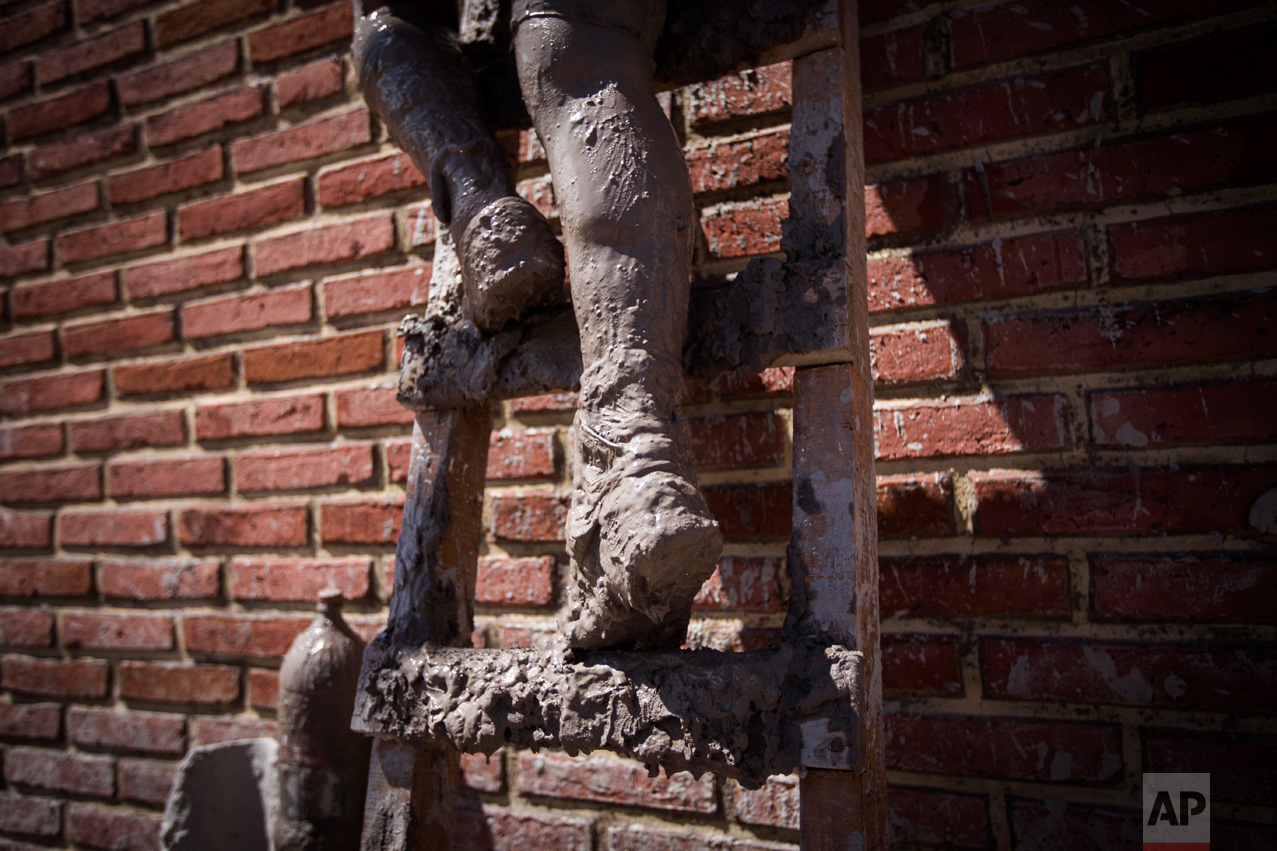 In this Jan. 13, 2017 photo, a local resident climbs a ladder as he carries his belongings to the roof of his mud damaged home, in the town of Volcan, Jujuy province, Argentina. Authorities declared the area a disaster zone after the town was hit by a mudslide one week ago, that covered it in a thick layer of mud. (Gianni Bulacio/Infoto via AP)