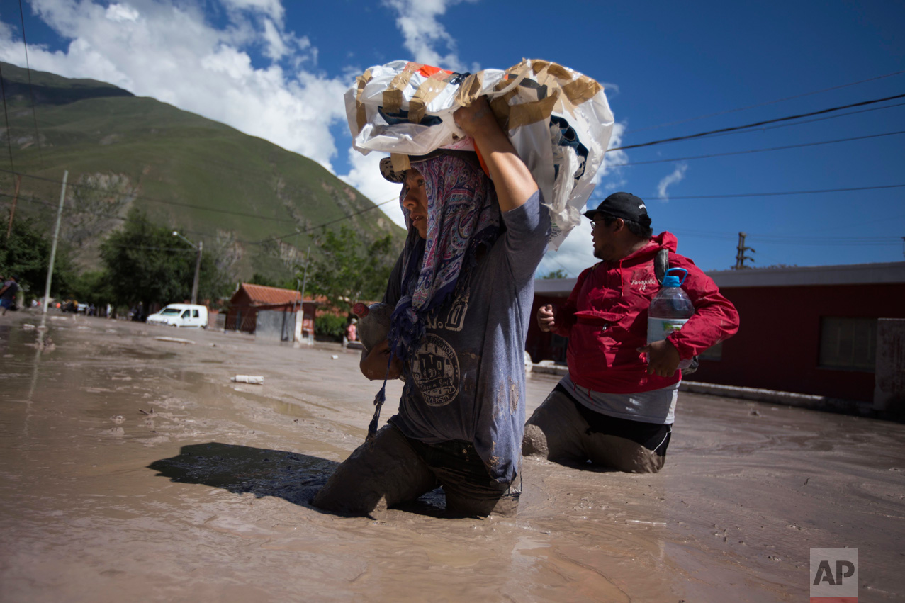 In this Jan. 13, 2017 photo, residents wade waist deep in the mud, with rescued religious figures, in the town of Volcan, Jujuy province, Argentina. The statues will be taken to a secure place until cleanup efforts are completed. (Gianni Bulacio/Infoto via AP)