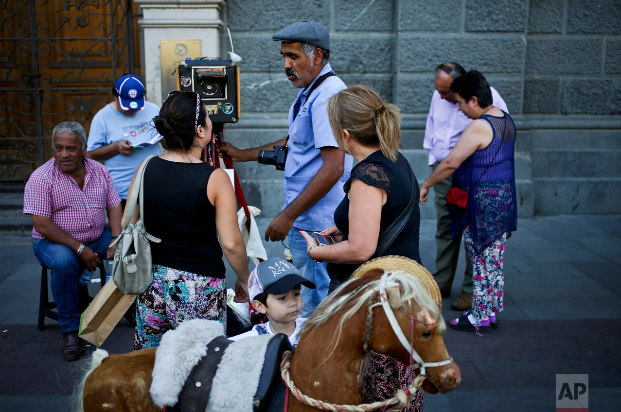In this Dec. 1, 2016 photo, photographer Luis Maldonado talks to a client next to his old wooden box camera in Plaza de Armas of Santiago, Chile. Because most people are unwilling to pay more for a box camera photograph, Maldonado ultimately had to buy a digital camera and a small printer to make cheaper photographs. (AP Photo/Esteban Felix)