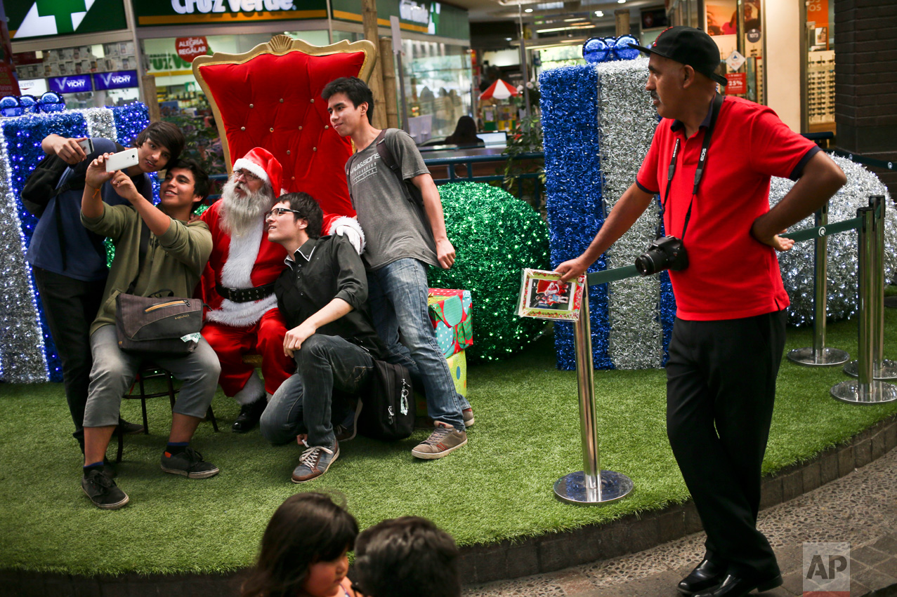 In this Dec. 18, 2016 photo, people take a selfie with Santa Claus as photographer Luis Maldonado waits for more clients at a mall in Santiago, Chile. Maldonado, the last remaining photographer in the main square of the Chilean capital still using a wooden box camera, has taken on other jobs to make ends meet. (AP Photo/Esteban Felix)
