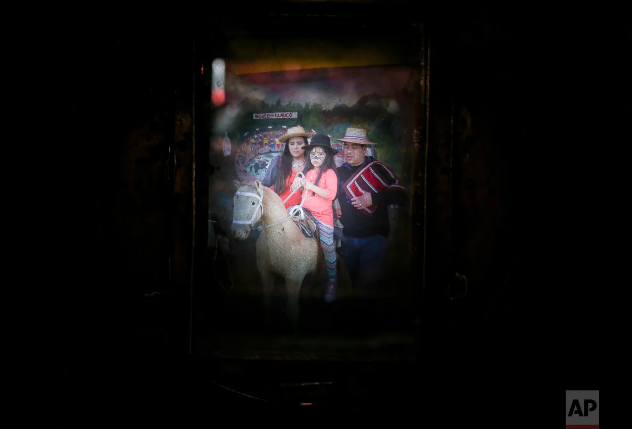 In this Sept. 4, 2016 photo, a family having their portrait taken fills the viewfinder of Luis Maldonado's old wooden old box camera, during a fair marking Independence Day in Santiago, Chile. At about $7.50 per portrait, a box camera photograph costs more than twice as much as the $3 charged for a digital one. (AP Photo/Esteban Felix)