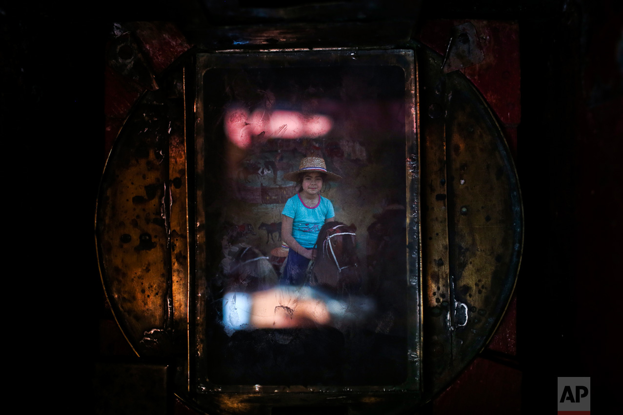 In this Sept. 4, 2016 photo, a girl getting her portrait made on a stuffed horse fills the viewfinder of Luis Maldonado's old wooden old box camera, during a fair marking Independence Day in Santiago, Chile. Maldonado believes box photography could be revived in Chile and wants to help raise awareness about the art form. (AP Photo/Esteban Felix)