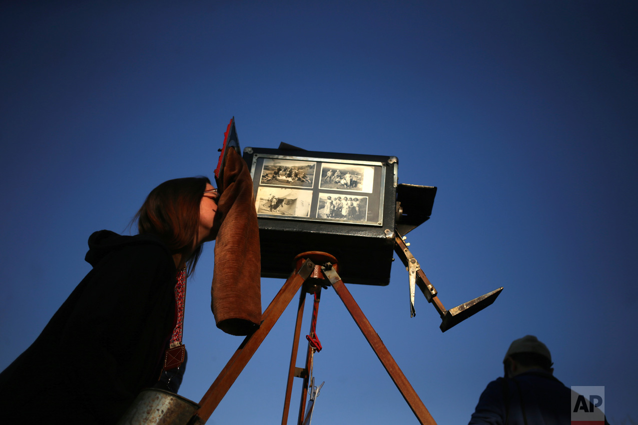 In this Sept. 4, 2016 photo, a woman looks through the viewfinder of the old wooden box camera used by photographer Luis Maldonado during a fair marking Independence Day in Santiago, Chile. Chile's box photographers union had more than 5,000 members by 1942, but that number plunged to about 300 by 1972, according to Chilean historian Octavio Cornejo. (AP Photo/Esteban Felix)