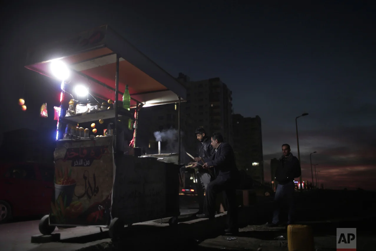 In this Monday, Jan. 16, 2017 photo, men buy hot corn from a street vendor at the side of a dark road during a power cut in Gaza City. (AP Photo/ Khalil Hamra)