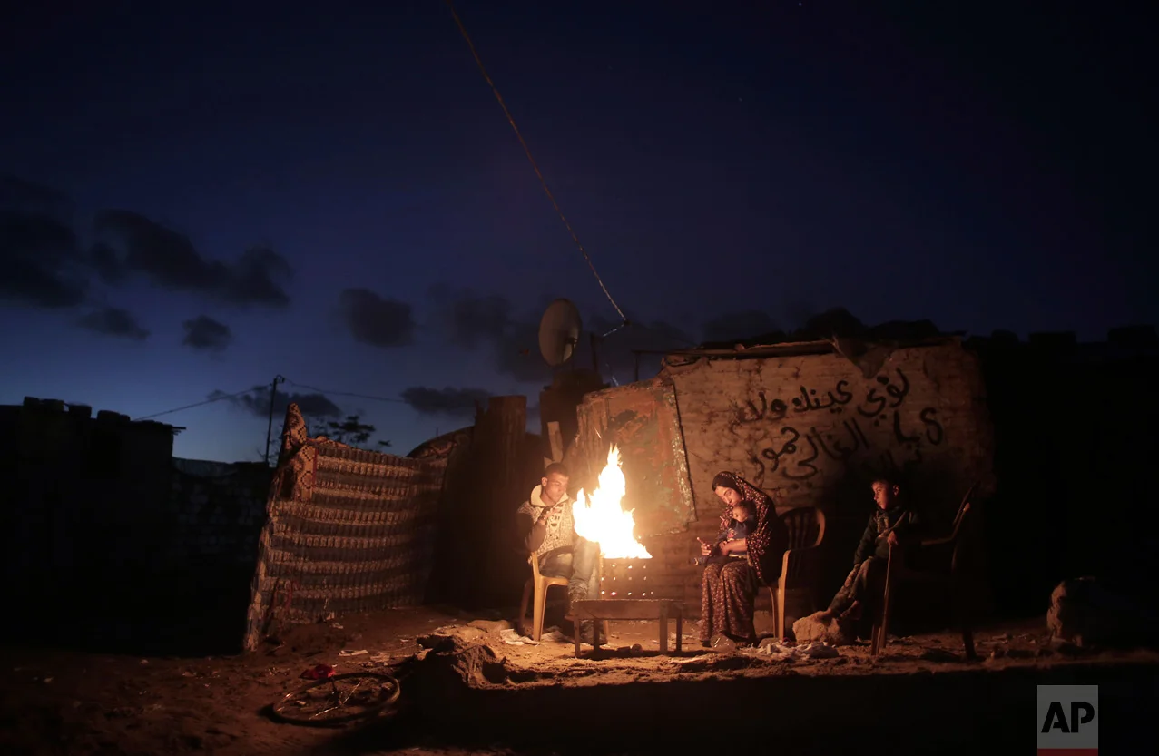 In this Sunday, Jan. 15, 2017 photo, a Palestinian family warm themselves up with a fire outside their makeshift house during a power cut in a poor neighborhood in town of Khan Younis in the southern Gaza Strip. (AP Photo/ Khalil Hamra)