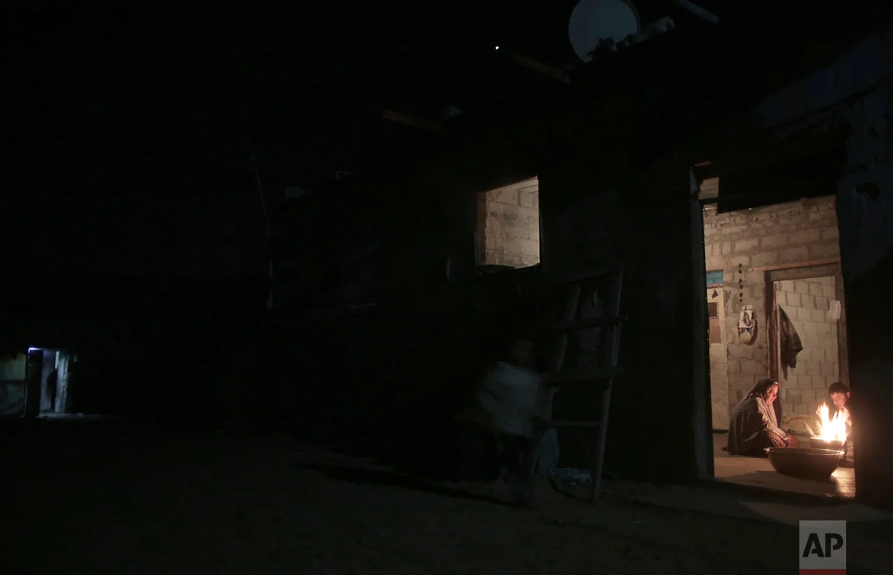 In this Sunday, Jan. 15, 2017 photo, a Palestinian family warm themselves up with a fire inside their makeshift house during the power cut in a poor neighborhood in town of Khan Younis in the southern Gaza Strip. (AP Photo/ Khalil Hamra)