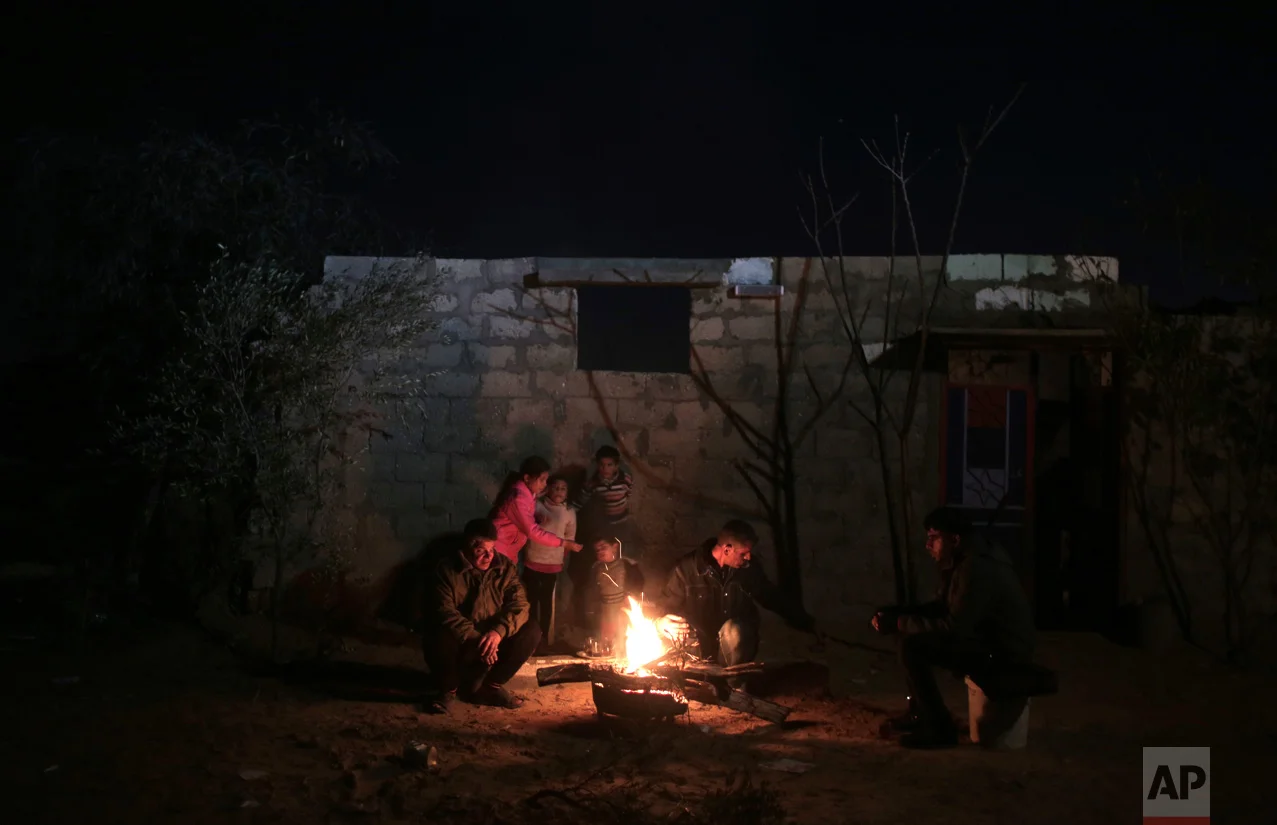 In this Sunday, Jan. 15, 2017 photo, a family warm themselves up with a fire outside their makeshift house during the power cut in a poor neighborhood in town of Khan Younis in the southern Gaza Strip. (AP Photo/ Khalil Hamra)