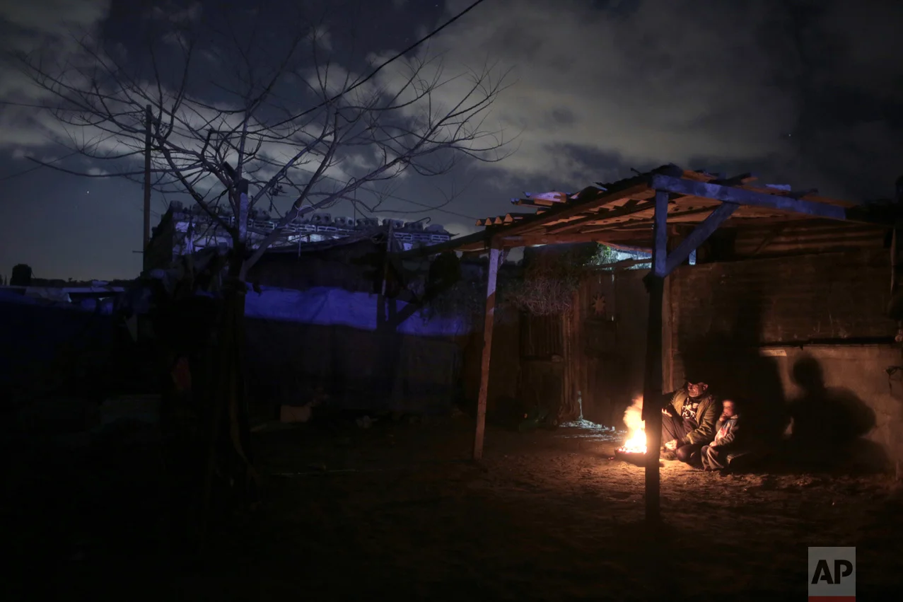 In this Sunday, Jan. 15, 2017 photo, a Palestinian family warm themselves up with a fire outside their makeshift house during the power cut in a poor neighborhood in town of Khan Younis in the southern Gaza Strip. (AP Photo/ Khalil Hamra)