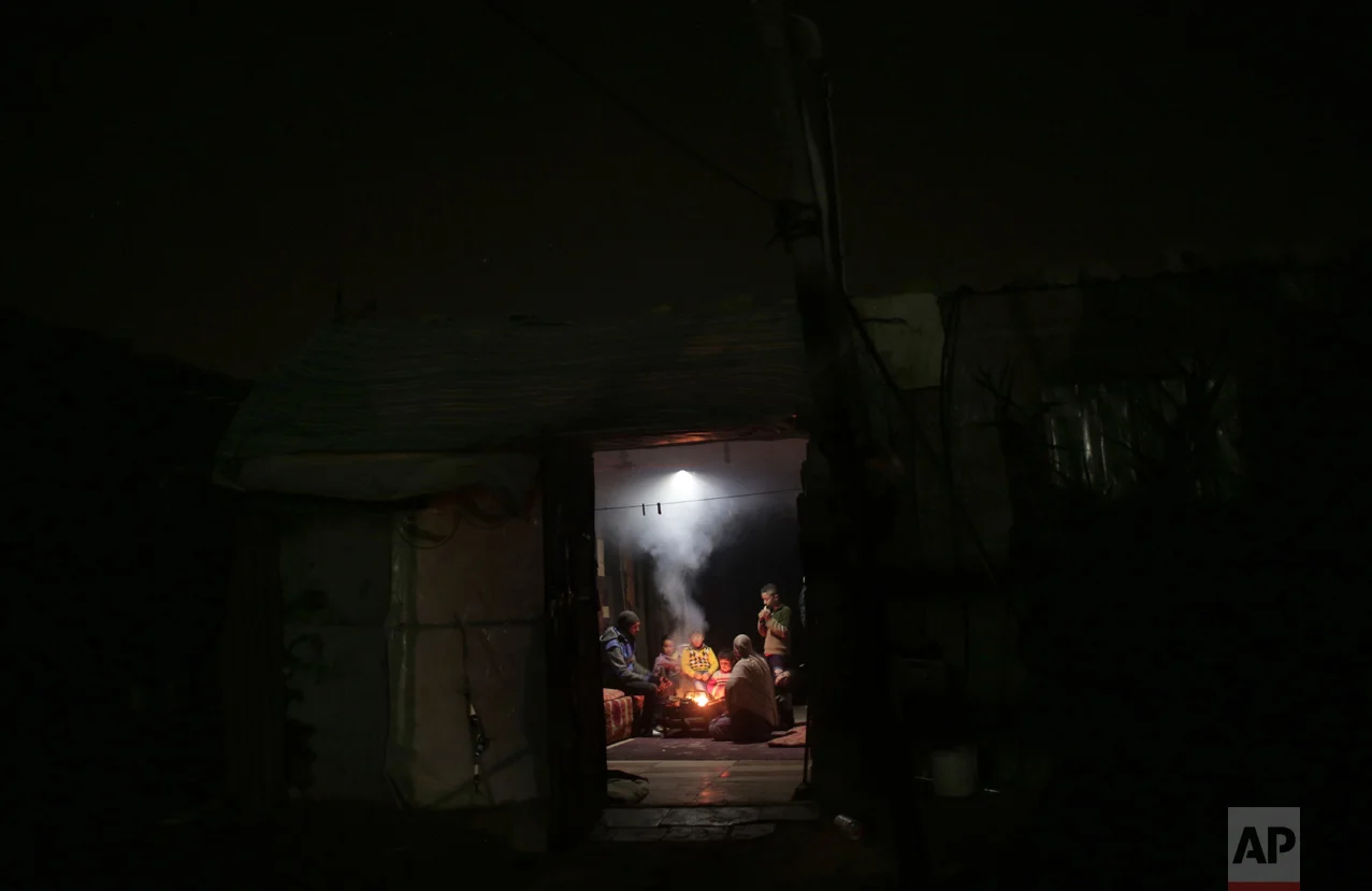 In this Sunday, Jan. 15, 2017 photo, a Palestinian family warm themselves up with a fire inside their makeshift house during the power cut in a poor neighborhood in town of Khan Younis in the southern Gaza Strip. (AP Photo/ Khalil Hamra)