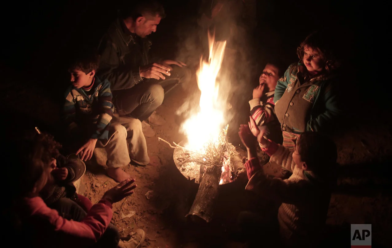 In this Sunday, Jan. 15, 2017 photo, a Palestinian family warm themselves up with a fire outside their makeshift house during the power cut in a poor neighborhood in town of Khan Younis in the southern Gaza Strip. (AP Photo/ Khalil Hamra)