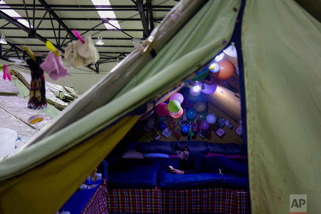 In this Tuesday, Jan. 17, 2017 photo, Syrian refugee Kawa Mohammed, 34, checks his mobile phone while laying inside his tent in Kalochori refugee camp on the outskirts of the northern Greek city of Thessaloniki. (AP Photo/Muhammed Muheisen)