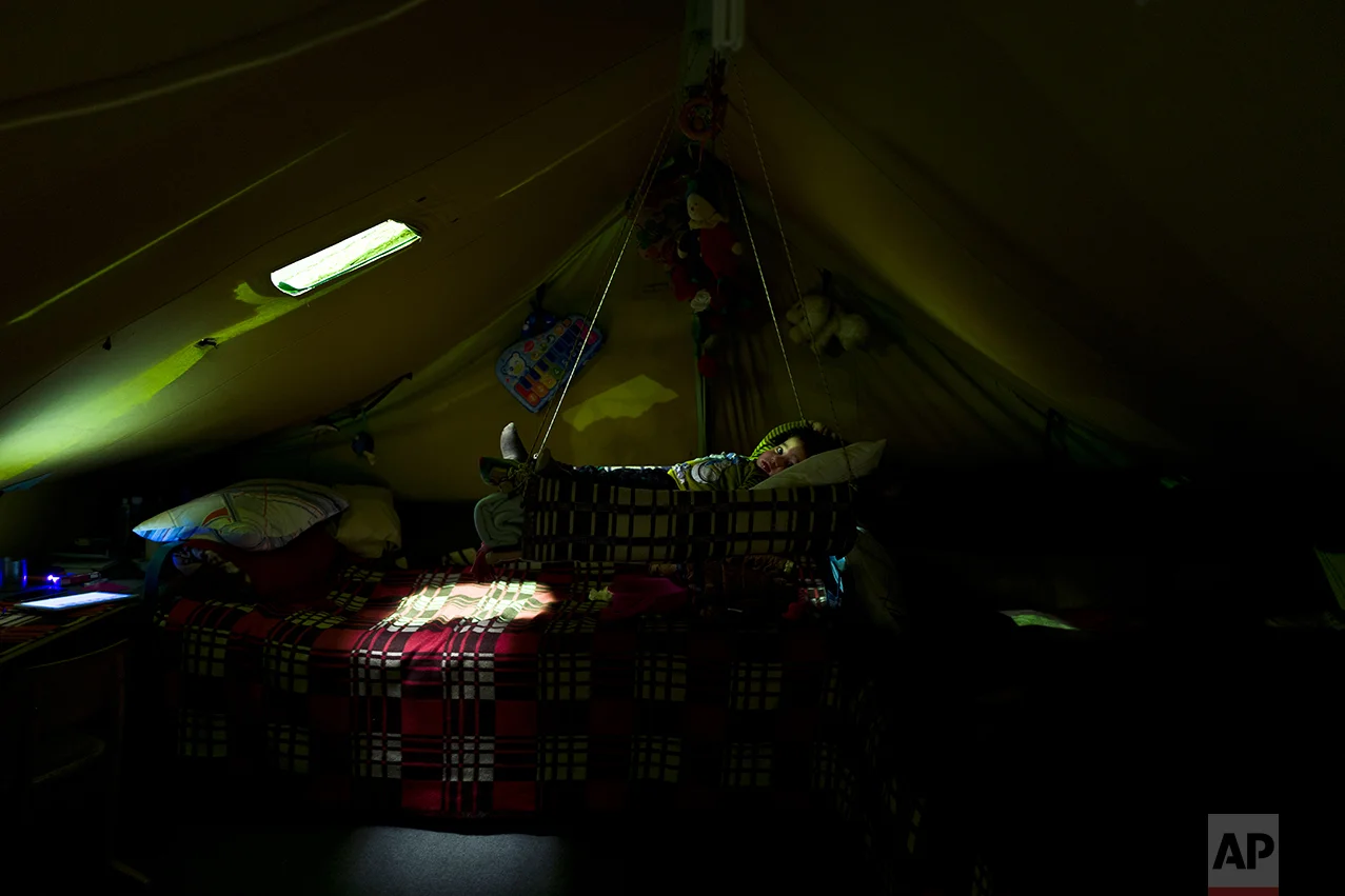 In this Tuesday, Jan. 17, 2017 photo, Mislina Moustafa, 2, a migrant from Diyarbakır, Turkey, lies in a hammock hanging from the sealing at her family's tent in Kalochori refugee camp on the outskirts of the northern Greek city of Thessaloniki. (AP Photo/Muhammed Muheisen)