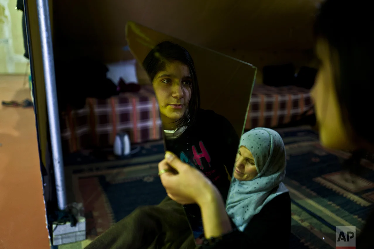 In this Tuesday, Jan. 17, 2017 photo, Syrian refugee Kulnawaz Youssef, 13, looks at herself in a mirror at her tent in Kalochori refugee camp on the outskirts of the northern Greek city of Thessaloniki. Many migrants living in this warehouse tent camp and another one nearby are feeling burned out. They try to keep busy as they dream of a better life in Western Europe and not let boredom or depression set in. (AP Photo/Muhammed Muheisen)