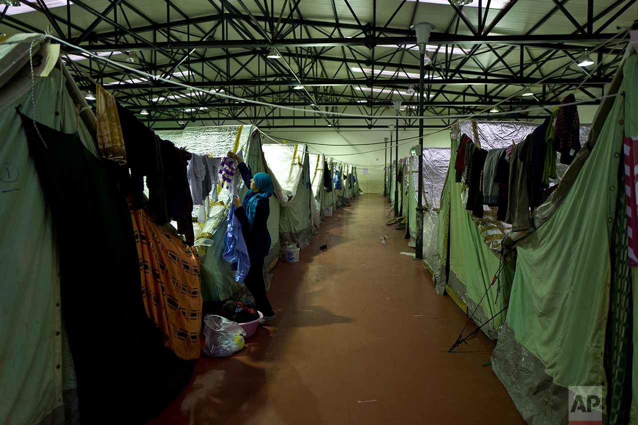 In this Tuesday, Jan. 17, 2017 photo, a Syrian refugee woman hangs her laundry outside her tent in Kalochori refugee camp on the outskirts of the northern Greek city of Thessaloniki. Because of a harsh winter and bitter cold, many migrants rarely venture out and away from the monotony and fluorescent lights hanging overhead. (AP Photo/Muhammed Muheisen)