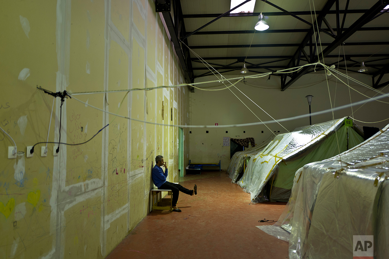 In this Tuesday, Jan. 17, 2017 photo, a Syrian refugee man smokes a cigarette near his tent in Kalochori refugee camp on the outskirts of the northern Greek city of Thessaloniki. Because of a harsh winter and bitter cold, many migrants rarely venture out and away from the monotony and fluorescent lights hanging overhead. (AP Photo/Muhammed Muheisen)