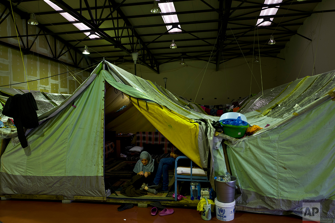 In this Tuesday, Jan. 17, 2017 photo, Syrian refugee Suad Abdulmajeed, 57, knits while sitting with her daughter at the entrance of their tent in Kalochori refugee camp on the outskirts of the northern Greek city of Thessaloniki. Many migrants living in this warehouse tent camp and another one nearby are feeling burned out. They try to keep busy as they dream of a better life in Western Europe and not let boredom or depression set in. (AP Photo/Muhammed Muheisen)