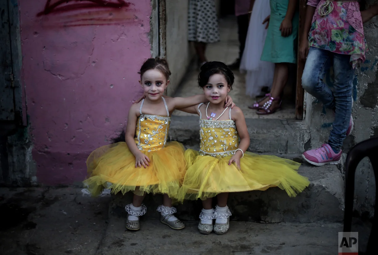 In this Saturday, July 30, 2016 photo, two girls pose for a picture as they sit in front of the family house during the wedding party of Palestinian groom Saed Abu Aser, in Gaza City. Weddings have emerged as a welcome celebration that slices through the often morose mood in the Gaza Strip, a Palestinian coastal territory run by the militant group Hamas. For both poor and well-off Gazans, weddings are a days-long, lavish affair of parties and dancing. (AP Photo/ Khalil Hamra)