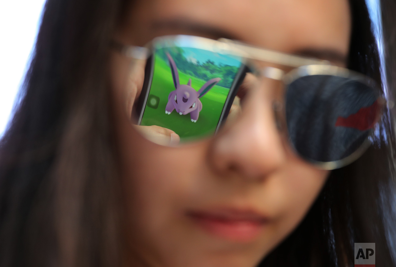 A mobile screen is reflected on a fan's sunglasses as she plays "Pokemon Go" in Hong Kong, Monday, July 25, 2016. Pokemon fans participated in creatures hunting on Monday as the app was released to both iPhone and Android users. (AP Photo/Kin Cheung)