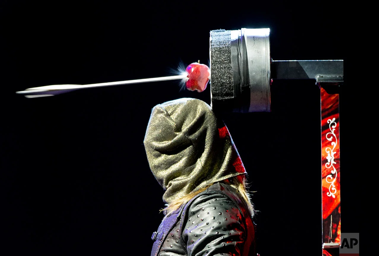 Ben Blaque, a crossbow sharpshooter, stands still after firing a crossbow wearing a hood, that then triggered a series of pre-set crossbows culminating in an arrow piercing the apple above his head, during a media event to promote the magic show, The Illusionists 1903, at the National Auditorium in Mexico City, Wednesday, July 13, 2016. The Illusionists 1903, evoking the "golden era" of magic shows, will be performed in Mexico City from July 13 to 24. (AP Photo/Rebecca Blackwell)