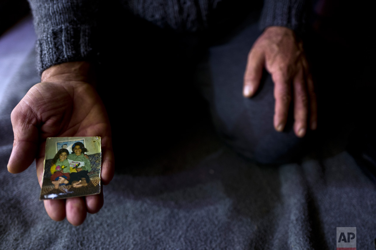 In this Thursday, Jan. 19, 2017 photo, Ibraheem Ghareeb, 55, a Syrian refugee from al-Zohour Street in Aleppo, shows a photograph of his daughters, Mariam, when she was 7-years-old and currently 20 and lives in Germany, and his late daughter Layla, 13, who passed away in 2004 back in Syria, at his tent in Kalochori refugee camp on the outskirts of the northern Greek city of Thessaloniki. "This is the only physical memory that I have left of my late daughter Layla, and it never leave my sight." Ibraheem said. (AP Photo/Muhammed Muheisen)