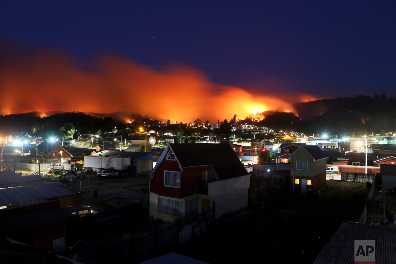 In this Monday, Jan. 30, 2017 photo, wildfires straddle Chile's Dichato community. Strong winds are continuing to stoke the flames of raging wildfires in Chile, forcing the evacuation of more than 800 families in the coastal town of Dichato. (AP Photo/Esteban Felix)