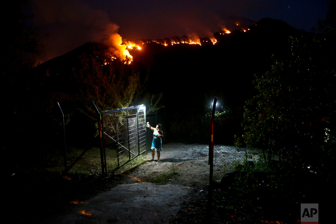 In this Tuesday, Jan. 24, 2017 photo, a woman closes a gate on her land as wildfires rage on a nearby mountain in Cajon del Maipo, on the outskirts of Santiago, Chile. Chile is suffering one of its worst fire disasters in history. The fires have outpaced local ability to put them out, forcing Chile to request international aid. (AP Photo/Esteban Felix)