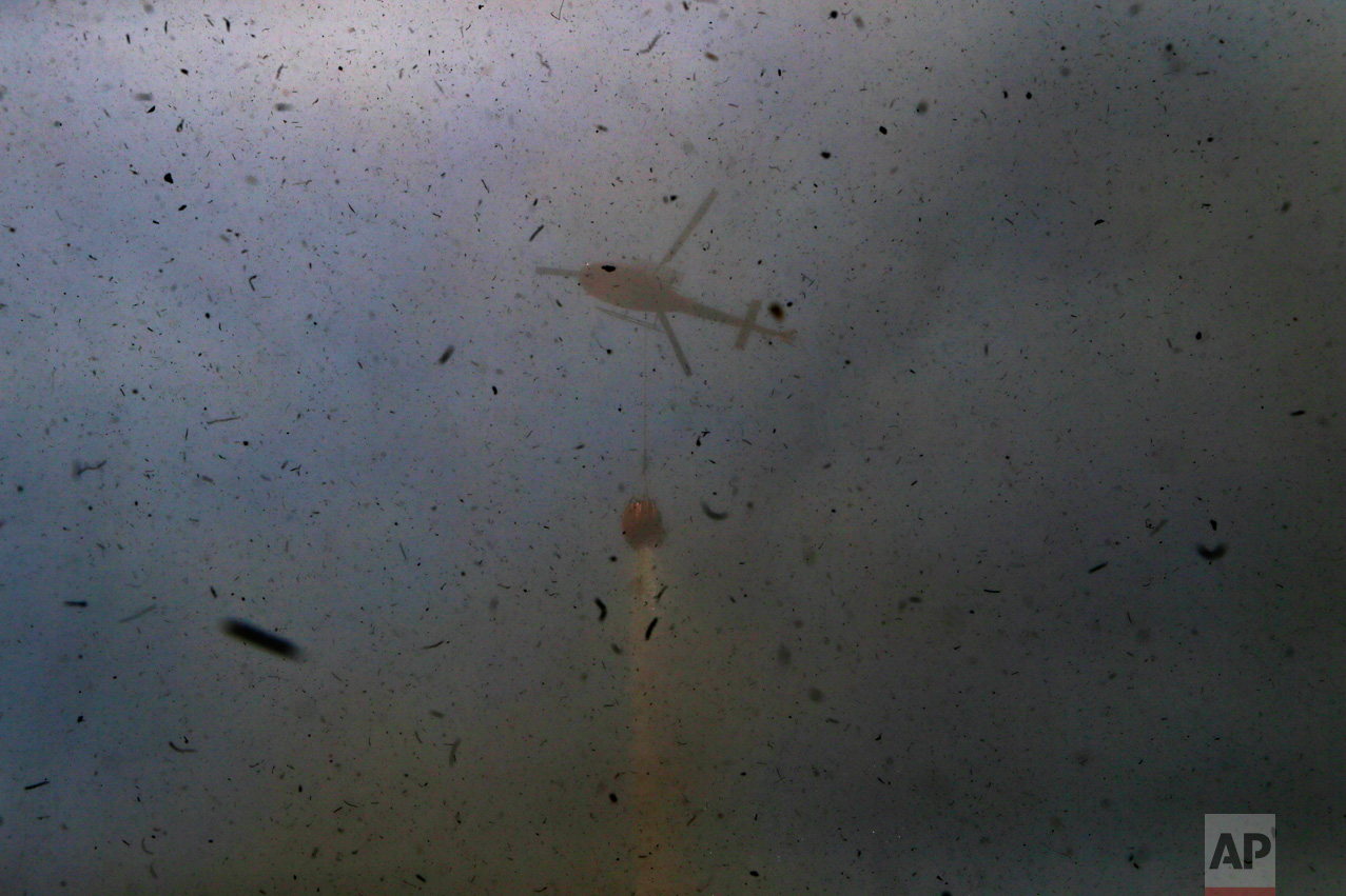 In this Sunday, Jan. 29, 2017 photo, debris is kicked up by a helicopter dumping water on wildfires in Portezuelo, Chile. Firefighters and residents are fighting the fast-spreading blazes on the ground, while a Russian supertanker plane and a Brazilian Hercules have dumped thousands of gallons of water, southwest of the Chilean capital. (AP Photo/Esteban Felix)