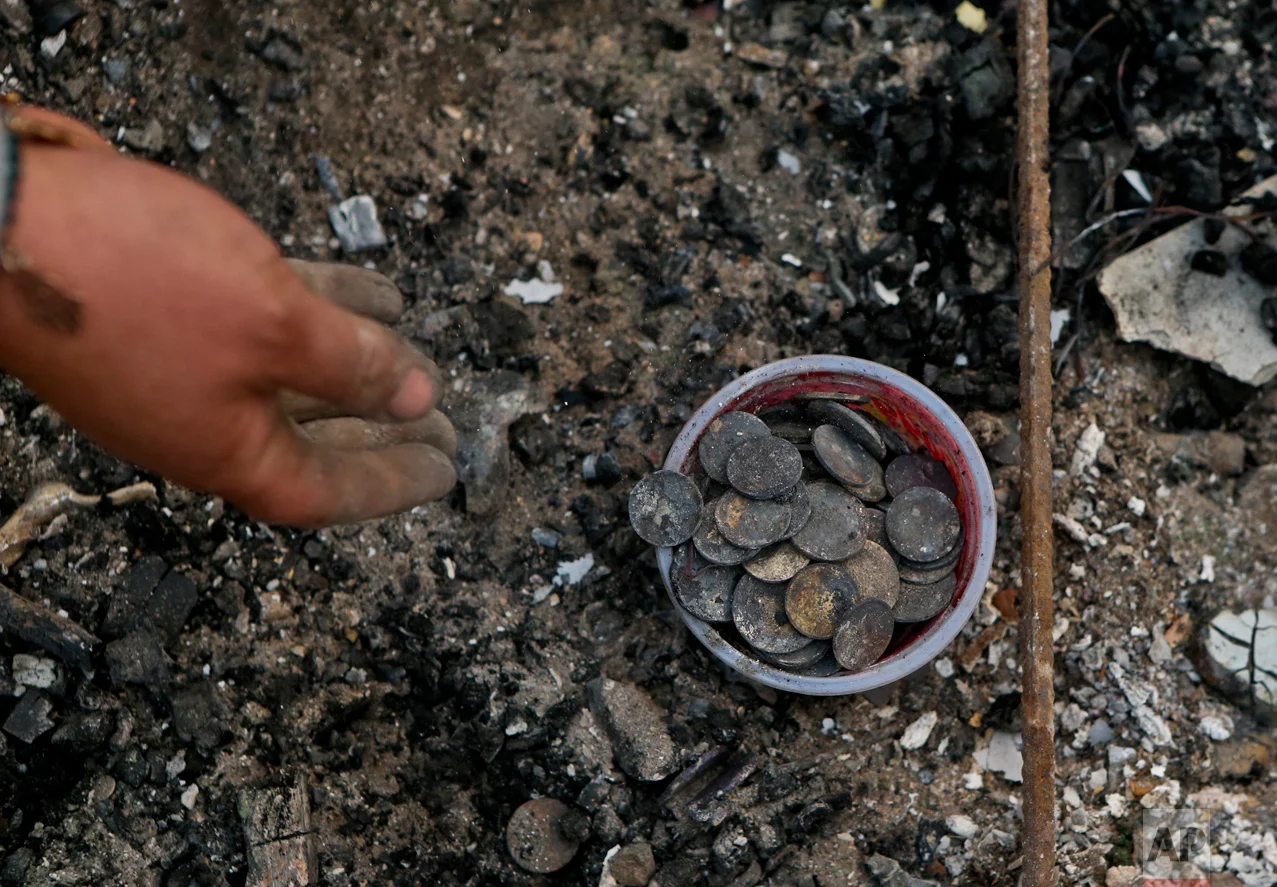 In this Thursday, Jan. 26, 2017 photo, Claudia Salinas salvages charred coins, which belong to her daughter, as she culls through the remains of their home destroyed by wildfires in Santa Olga, Chile. The flames engulfed the post office, a kindergarten, and about 1,000 homes in the town, located south of the Chilean capital. (AP Photo/Esteban Felix)
