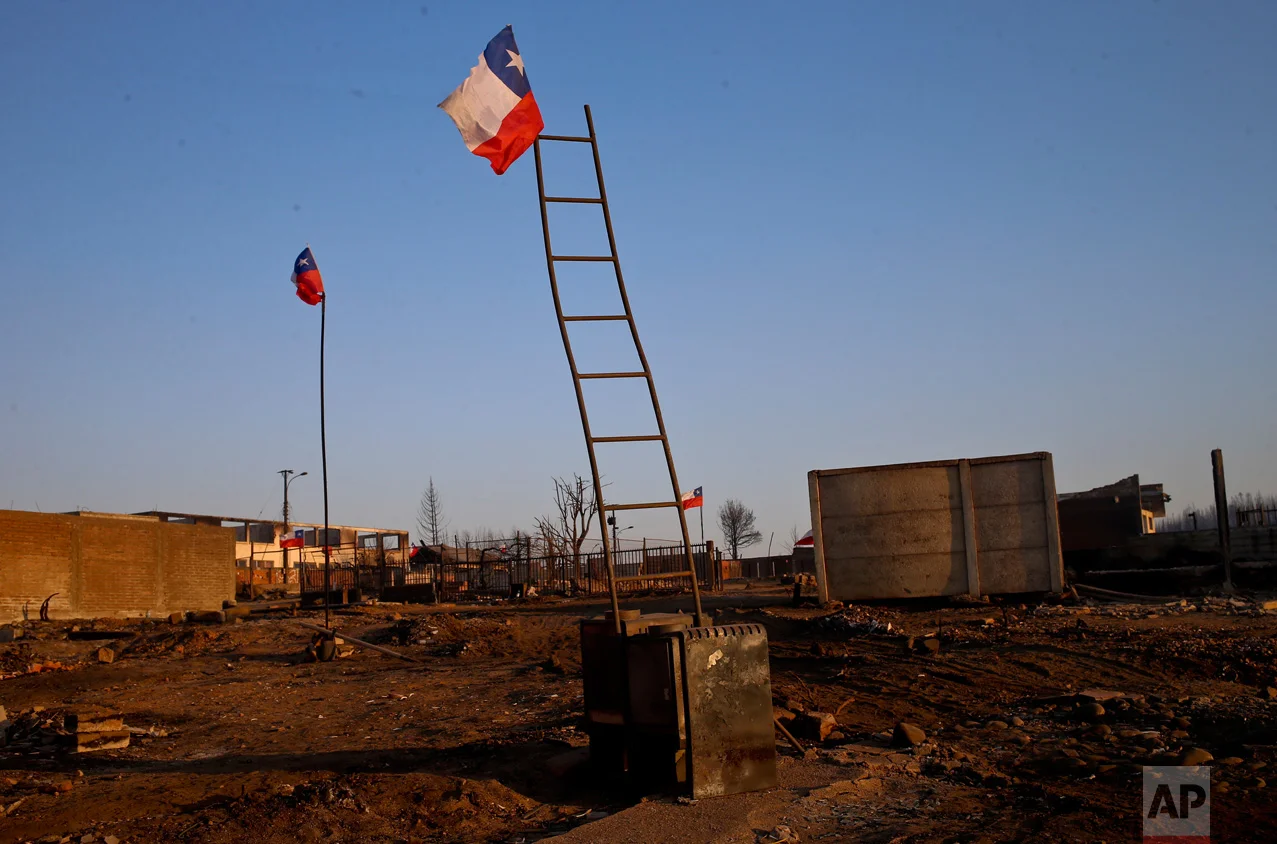 National flags fly over the scorched landscape of Chile's Santa Olga community, Tuesday, Jan. 31, 2017. The national forestry agency says Chile's raging wildfires have destroyed nearly 904,000 acres (366,000 hectares) since Jan. 15. (AP Photo/Esteban Felix)